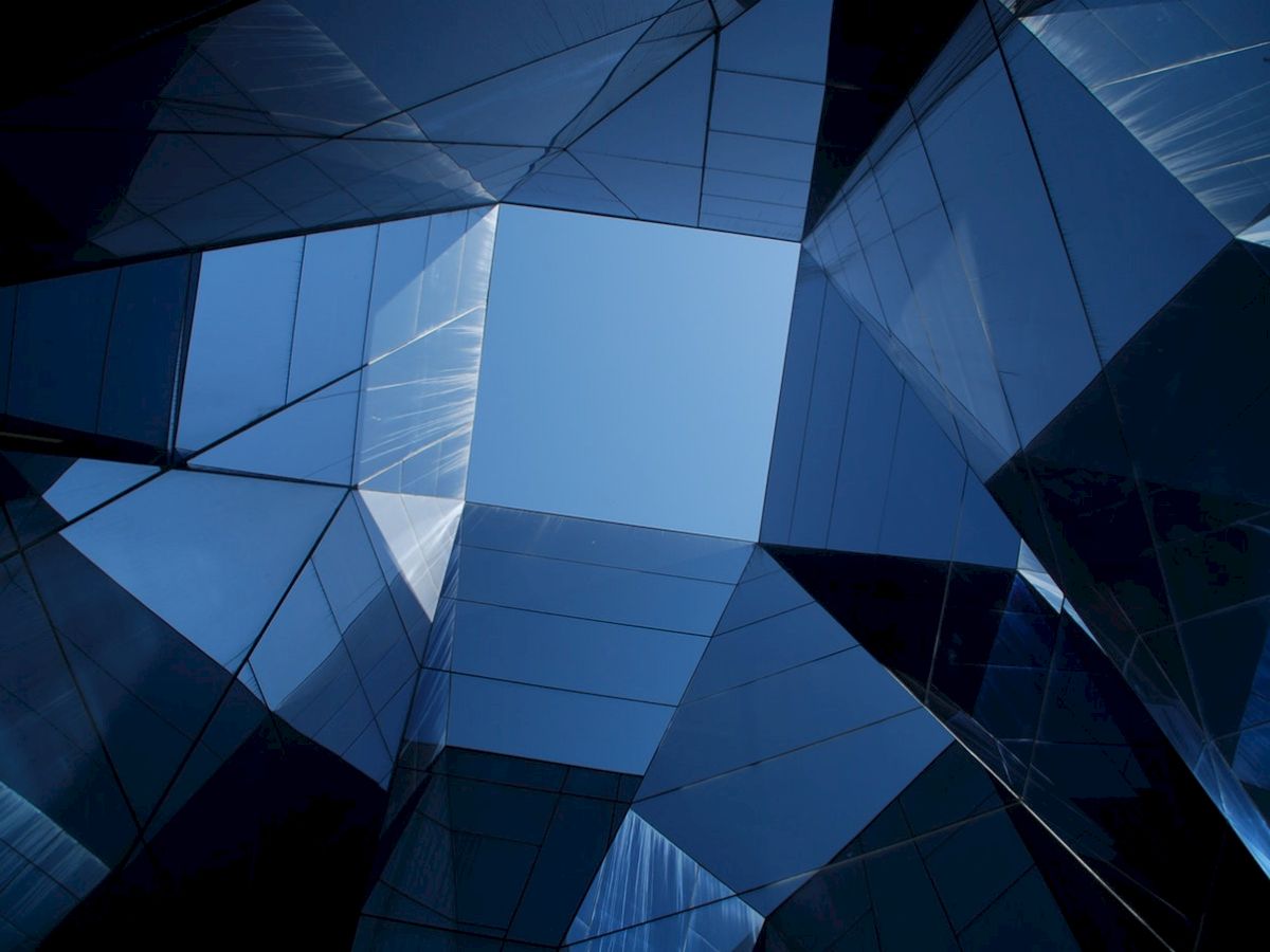 A view of modern architectural structures with reflective glass panels, creating a geometric pattern against the sky from a low angle.