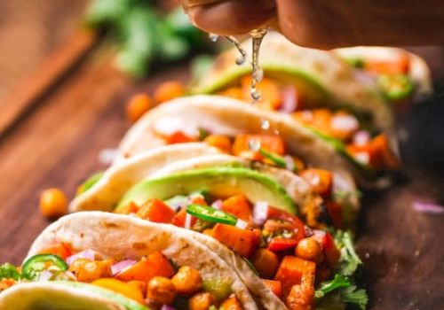 A hand squeezes lime over tacos filled with chickpeas, avocado, and veggies on a wooden board, with lime slices in the foreground.