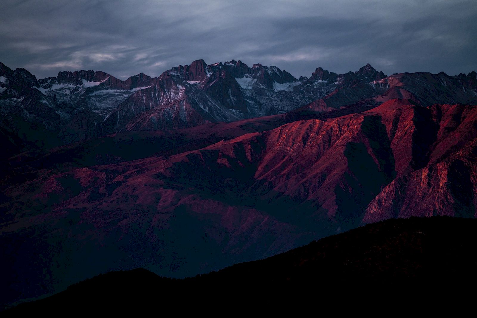A mountainous landscape under a dramatic sky, with red hues illuminating the peaks at sunset.