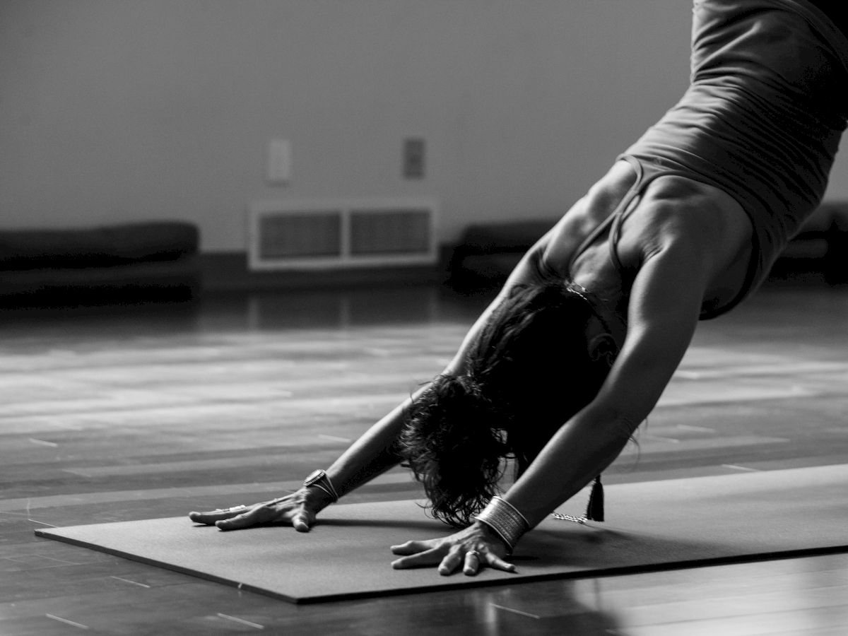 A person is performing a yoga pose, likely Downward Dog, on a mat in a dimly lit room.