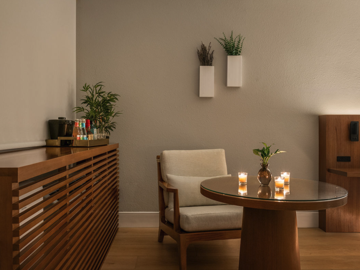 A cozy lounge area with a wooden chair and glass table lit by candles, plus plants and a wooden service counter.