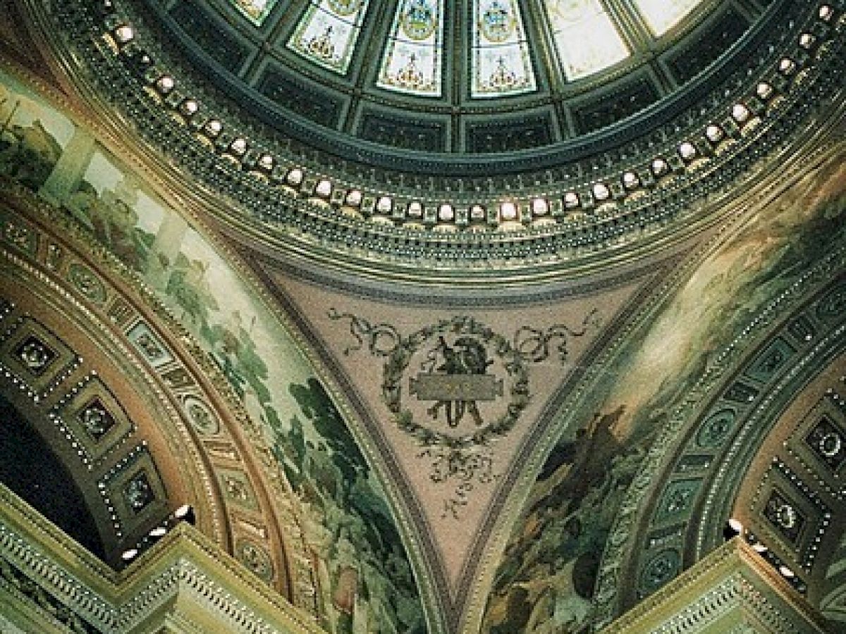 A decorative interior dome with stained glass, ornate murals, and detailed architectural elements, viewed from below.