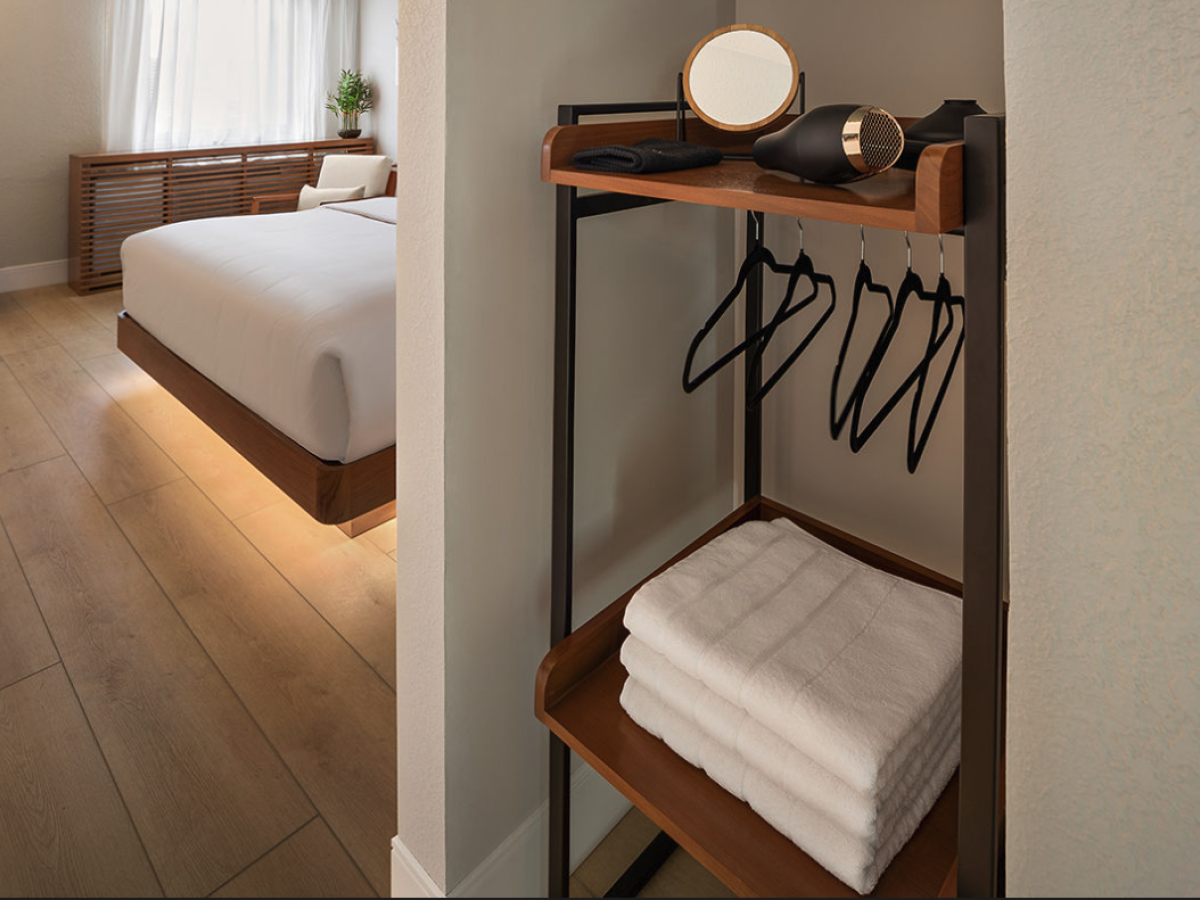 A modern bedroom with a neatly made bed and a clothes rack holding hangers, a hair dryer, and folded towels.