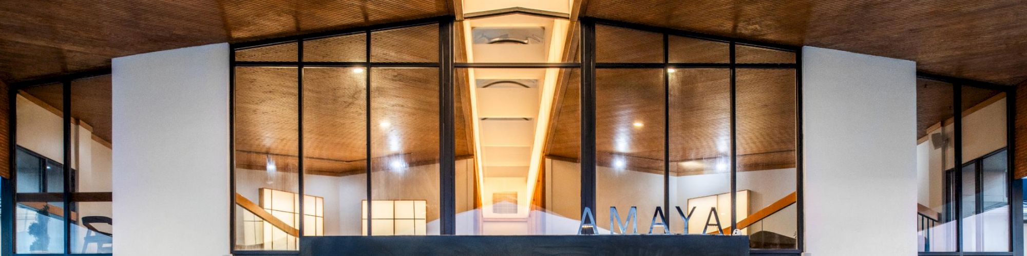 A modern building entrance with glass doors, brick and white columns, and warm interior lighting glowing through large windows.