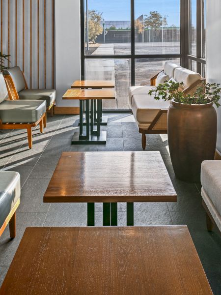 A modern lounge with comfy sofas, wooden tables, and soft natural light streaming through large windows, creating a calm, stylish vibe.