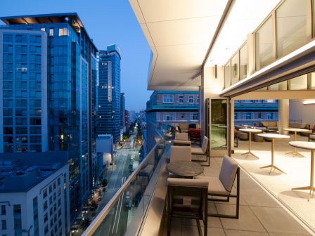 Cityscape from a modern balcony at dusk, featuring tall buildings and outdoor seating.