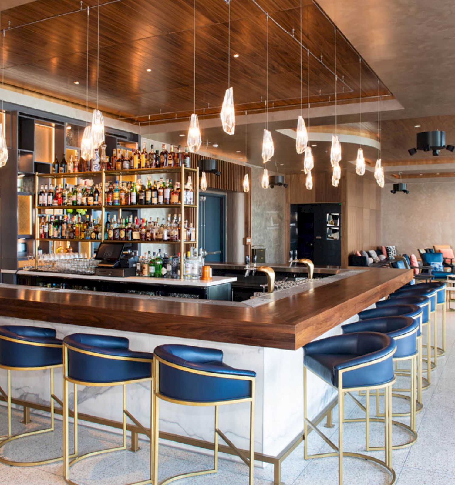 The image shows a modern bar with a sleek design, featuring a stocked bar, stylish seating, and overhead pendant lights.