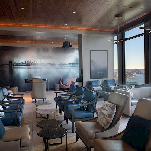A modern lounge with stylish seating, a city skyline mural, and large windows offering a scenic view of a body of water.
