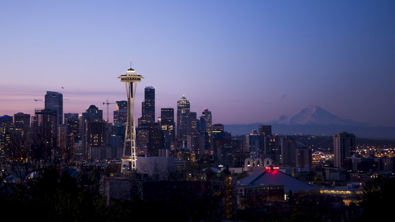 Seattle skyline at dusk with the Space Needle prominently visible and Mount Rainier in the background.
