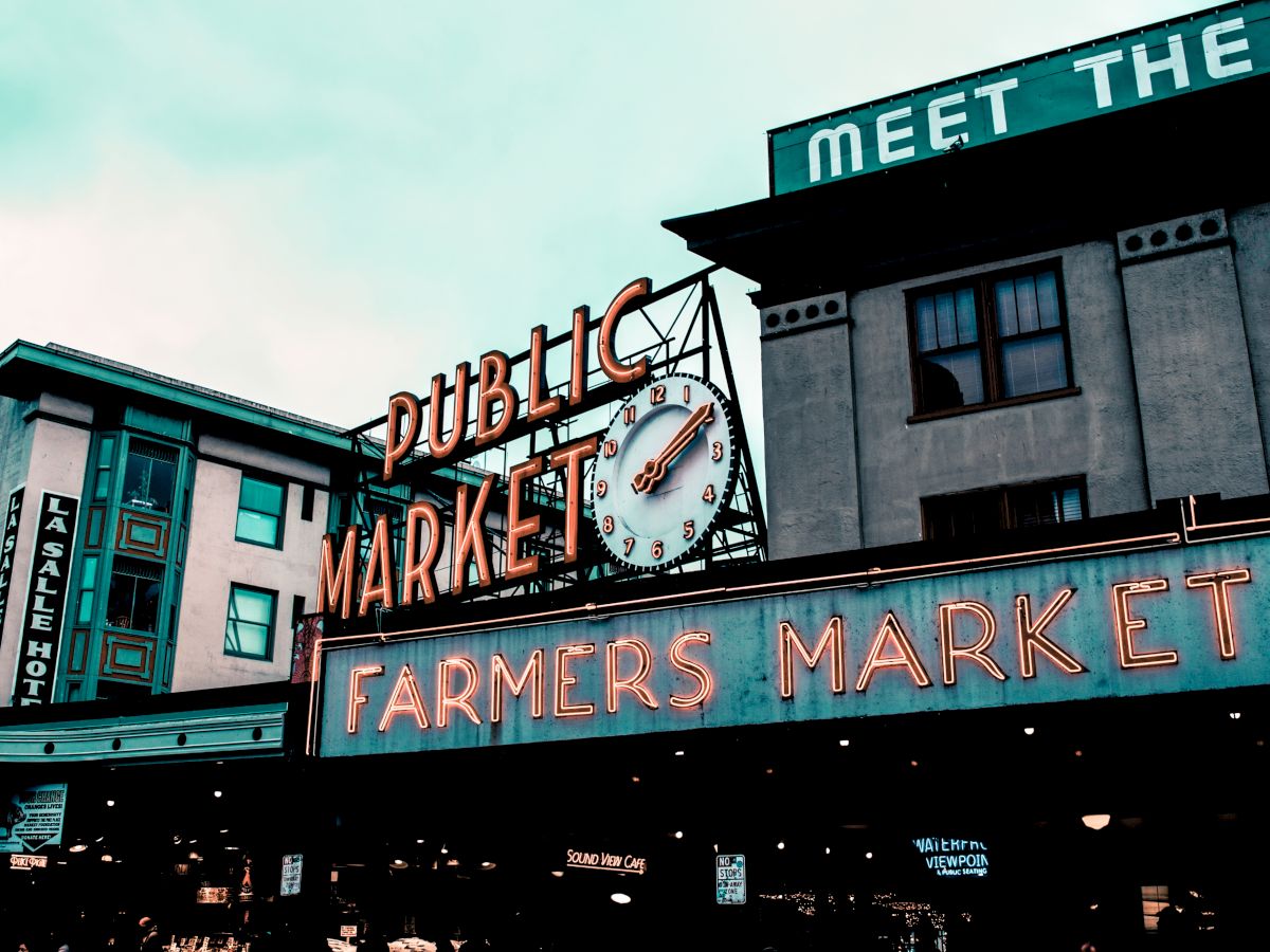 The image shows a public market with a neon sign reading "Farmers Market" and a clock, suggesting a bustling urban setting.